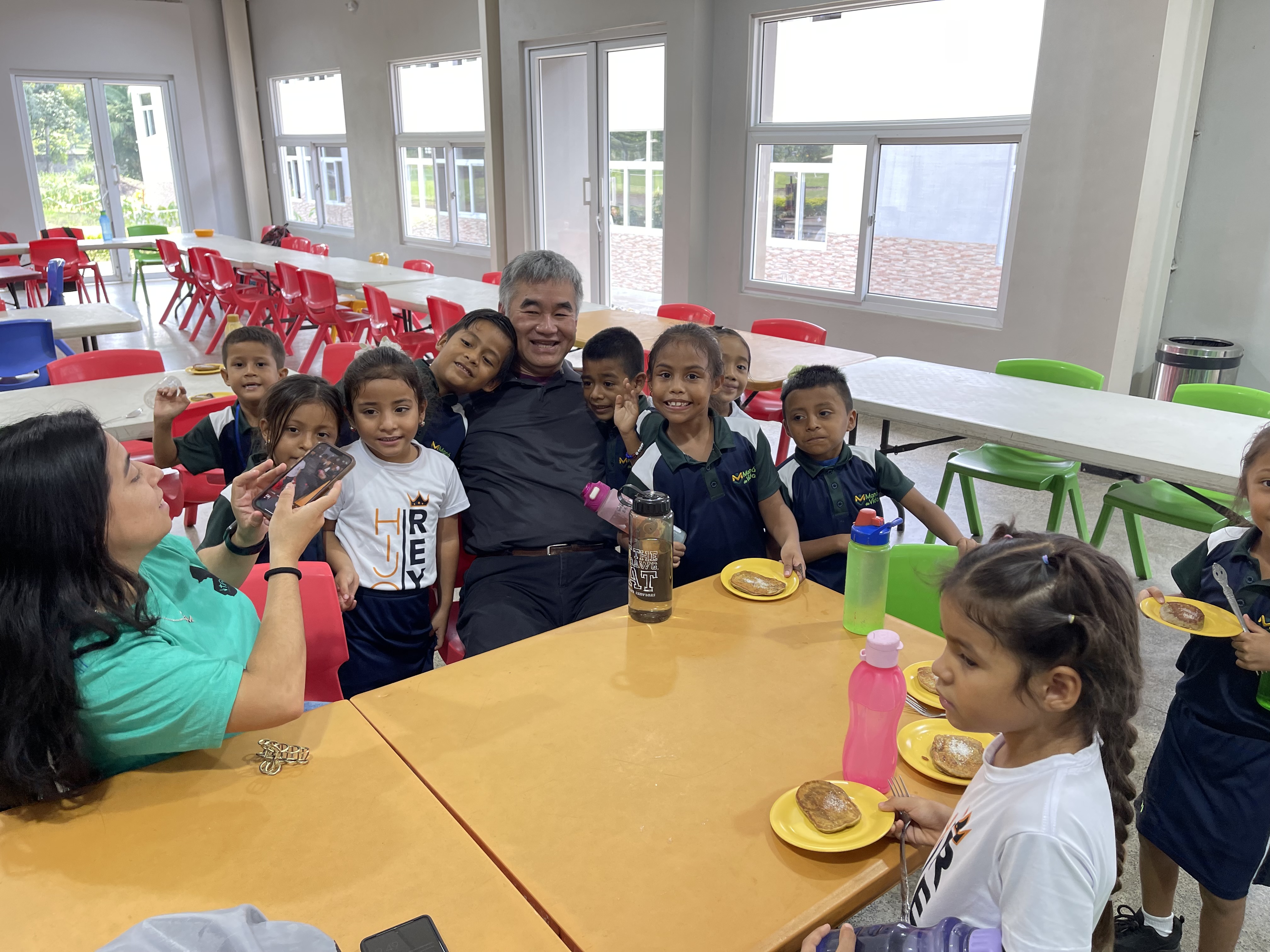 Thy sitting down with students at a desk at the Mana De Vida school in summer of 2022